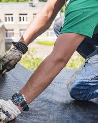 A construction worker cuts waterproofing material and prepares it for installation. Overhaul of the roof of the house.
